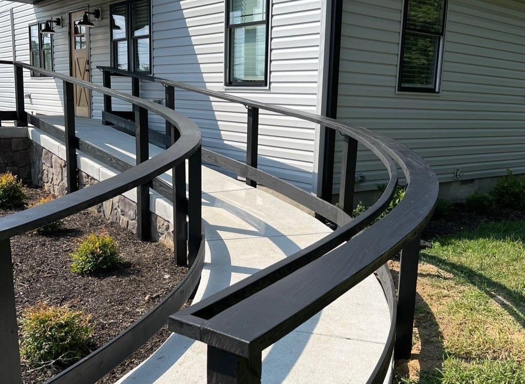 A view of a concrete ramp with a black railing curving up to a house.