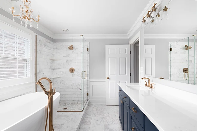 A beautiful bathroom with a blue vanity cabinet freestanding bathtub shower and gold faucets