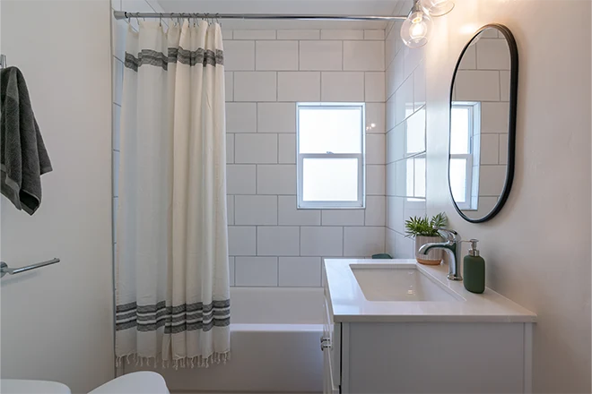Bathroom detail of large tiled tub with shower curtain small vanity and black rim mirror