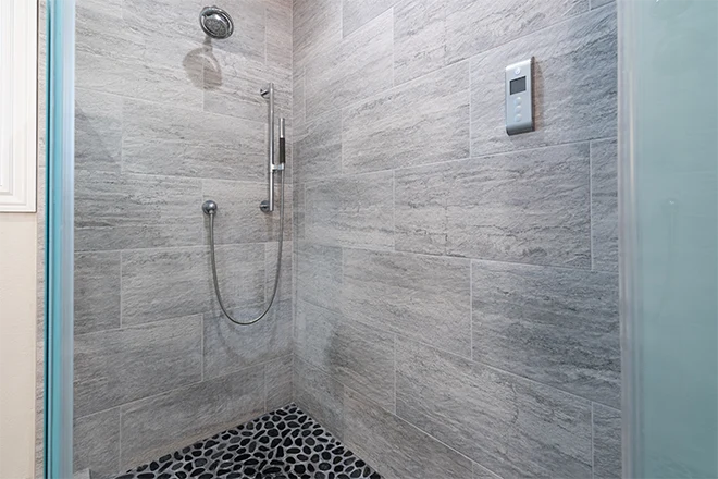 Walk-in shower with smooth gray tile walls and pebble rock flooring